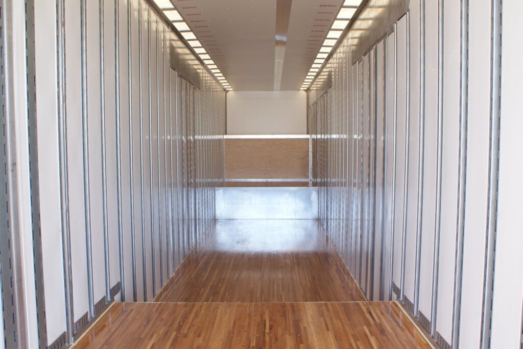 An empty cargo area of a truck showing wooden flooring and metal walls with a horizontal support bar.