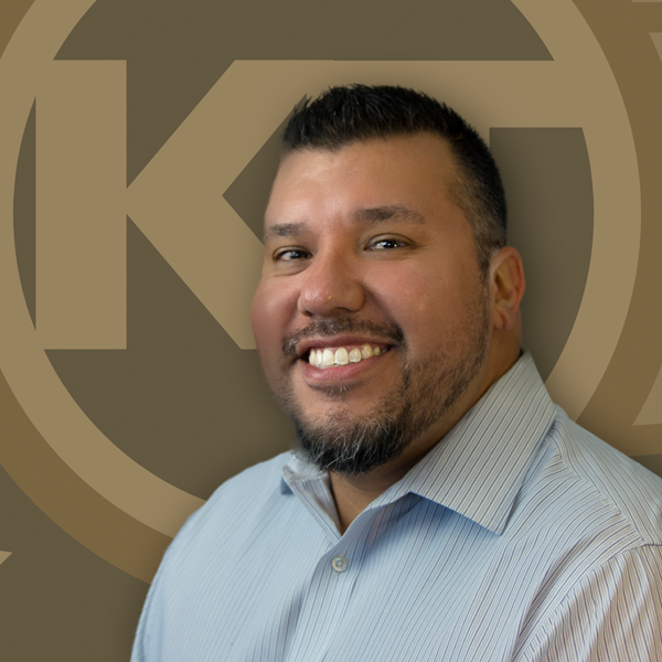 A smiling individual in professional attire is posing in front of a background with a circular design.