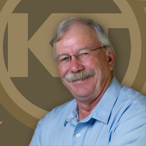 A smiling individual with a mustache is wearing a blue shirt and glasses, with a logo in the background.