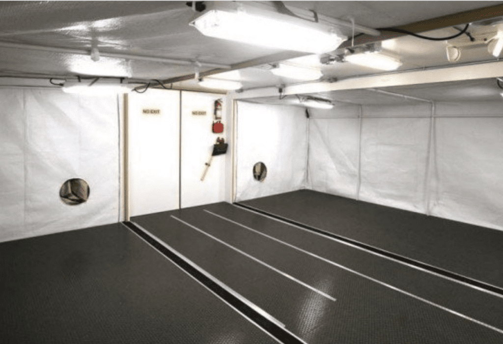 A clean and empty room is equipped with fluorescent lighting and what appears to be air ventilation ports on the walls.